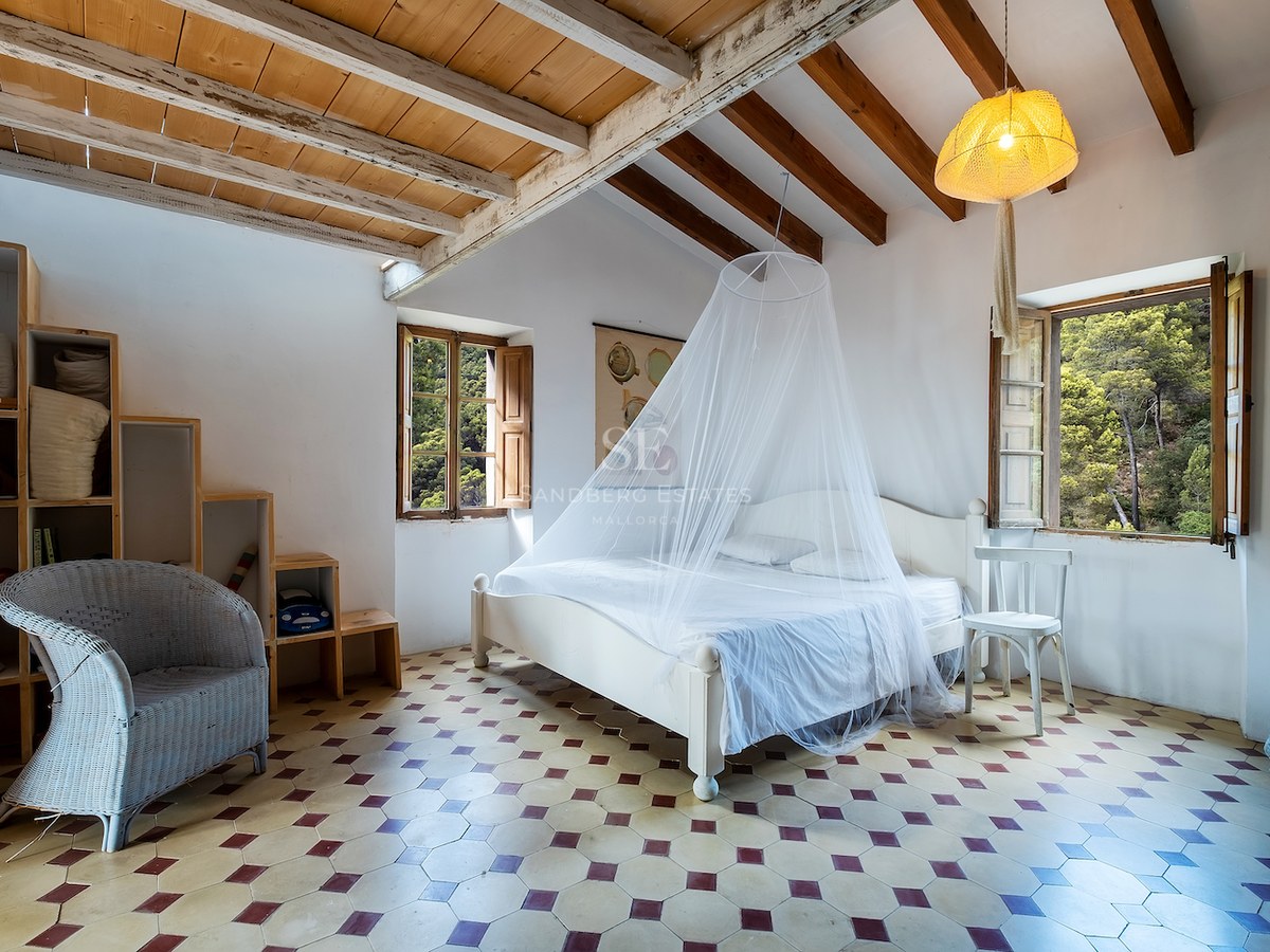 Chambre avec murs blancs, poutres en bois, sol en carrelage à motifs et lit avec moustiquaire.