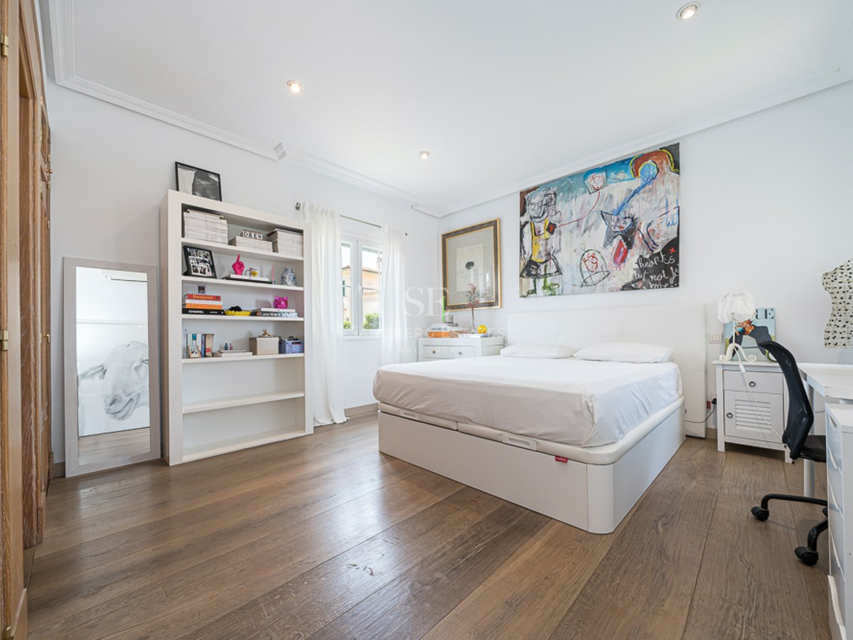 Chambre lumineuse avec murs blancs, parquet en bois, lit double, bibliothèque blanche et bureau.