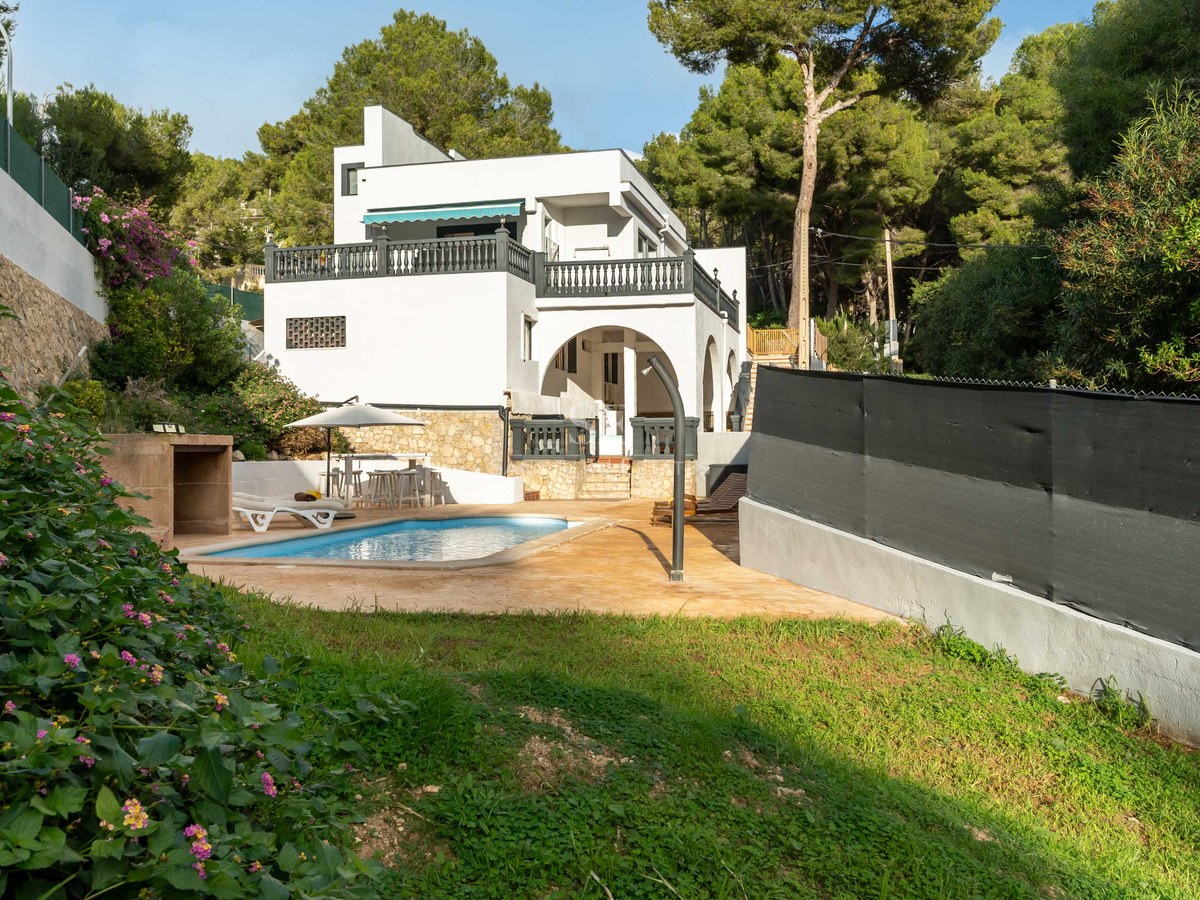 White multi-story villa featuring a private swimming pool, sun terrace, and lawn surrounded by a lush pine forest.