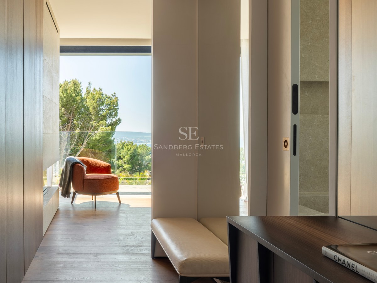 Couloir moderne, parquet en bois, fauteuil terracotta et grandes baies vitrées offrant une vue sur mer et pins.