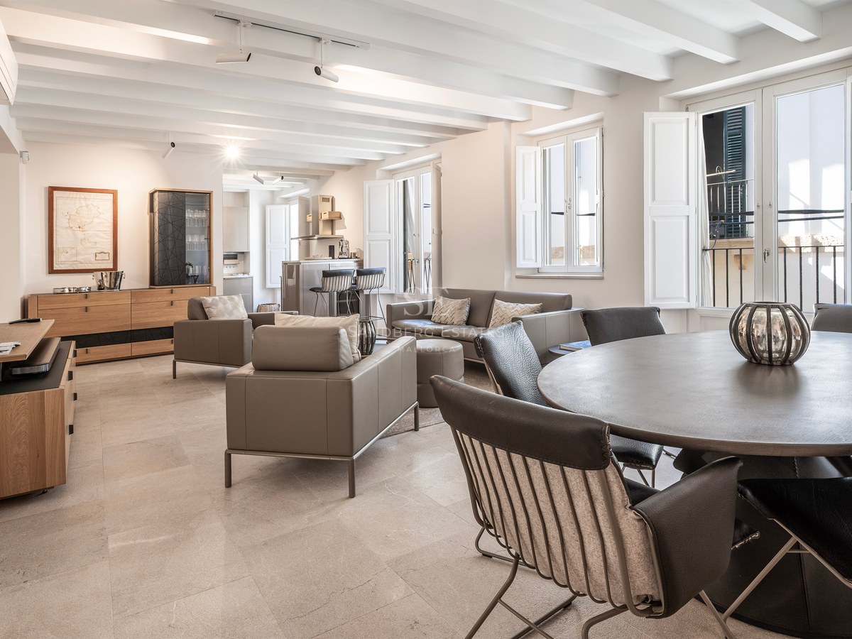 Spacious living room with white beamed ceilings, gray leather furniture, and a round dining table in the foreground.