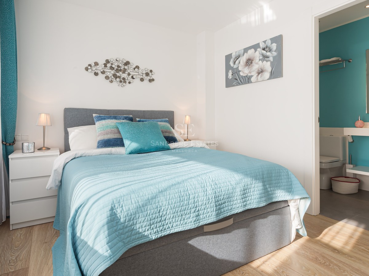 Bright bedroom featuring turquoise bedding, a grey upholstered headboard, and an open doorway to a matching ensuite bathroom.