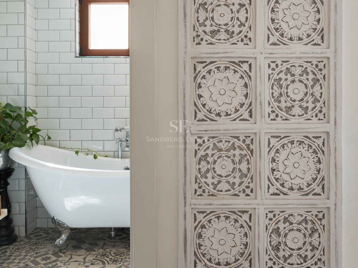 Un baño con bañera blanca de patas, azulejos tipo metro y suelo hidráulico, visto a través de una puerta de madera tallada.