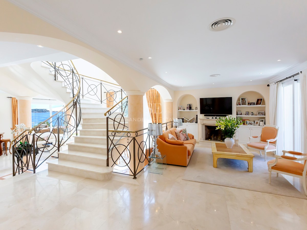 Spacious living room featuring a grand marble staircase, arched windows with sea views, and a classic fireplace.