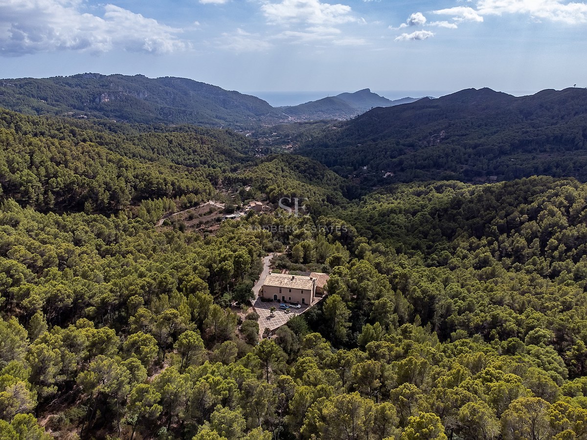 Vue aérienne d'une villa privée entourée d'une forêt verdoyante dans une vallée avec vue sur la mer au loin.