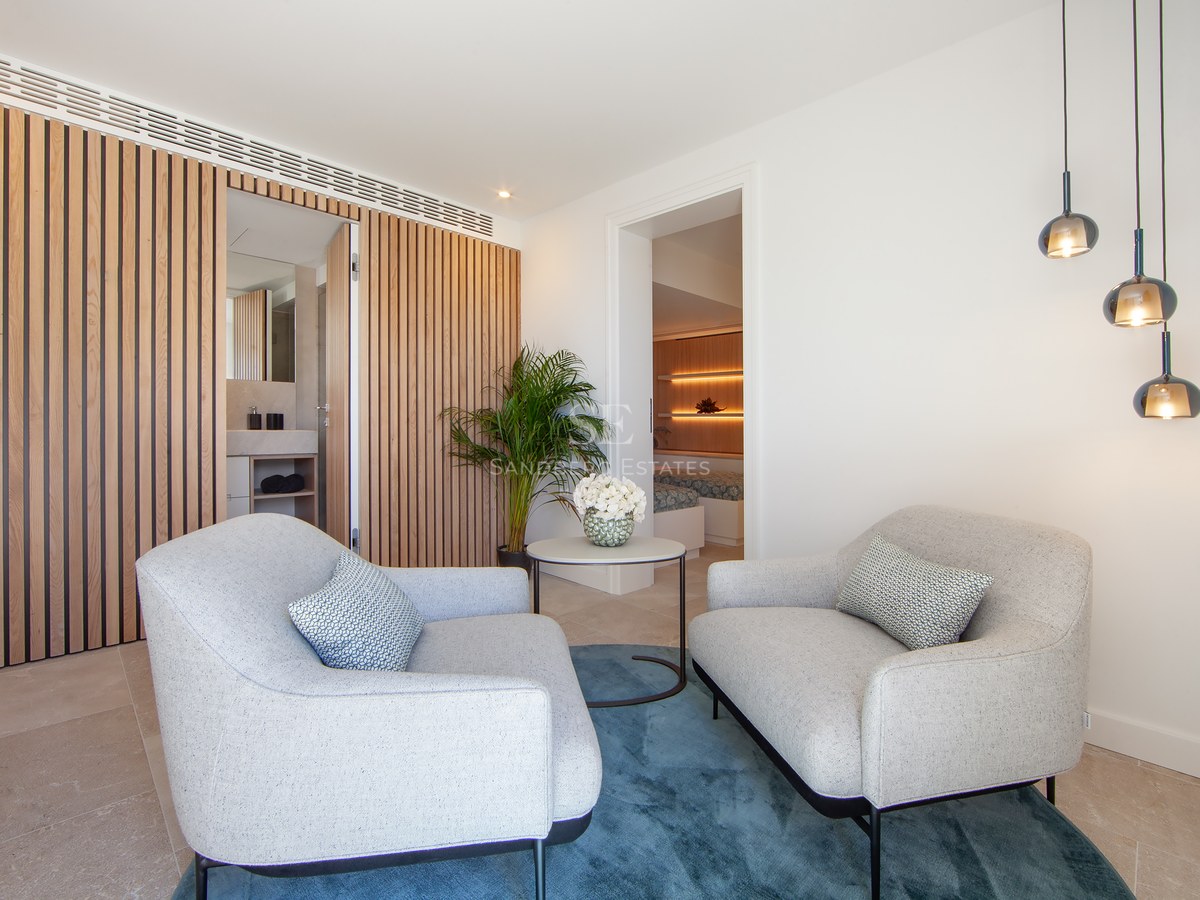 Master bedroom suite featuring two grey armchairs, blue rug, wooden slat wall, and view of the bedroom area.