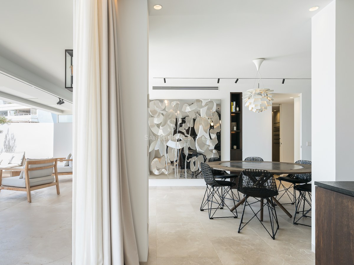 Salle à manger moderne avec table ronde en bois s'ouvrant sur une terrasse ensoleillée avec mobilier de salon.