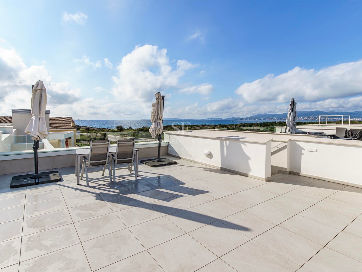 Grande terrasse moderne avec carrelage blanc, garde-corps en verre et coin repas avec vue sur la mer bleue.
