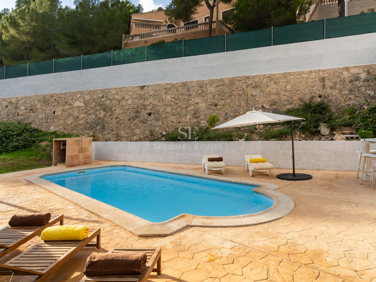 Outdoor pool with stone terrace, lounge chairs, white umbrella, and stone wall backdrop.