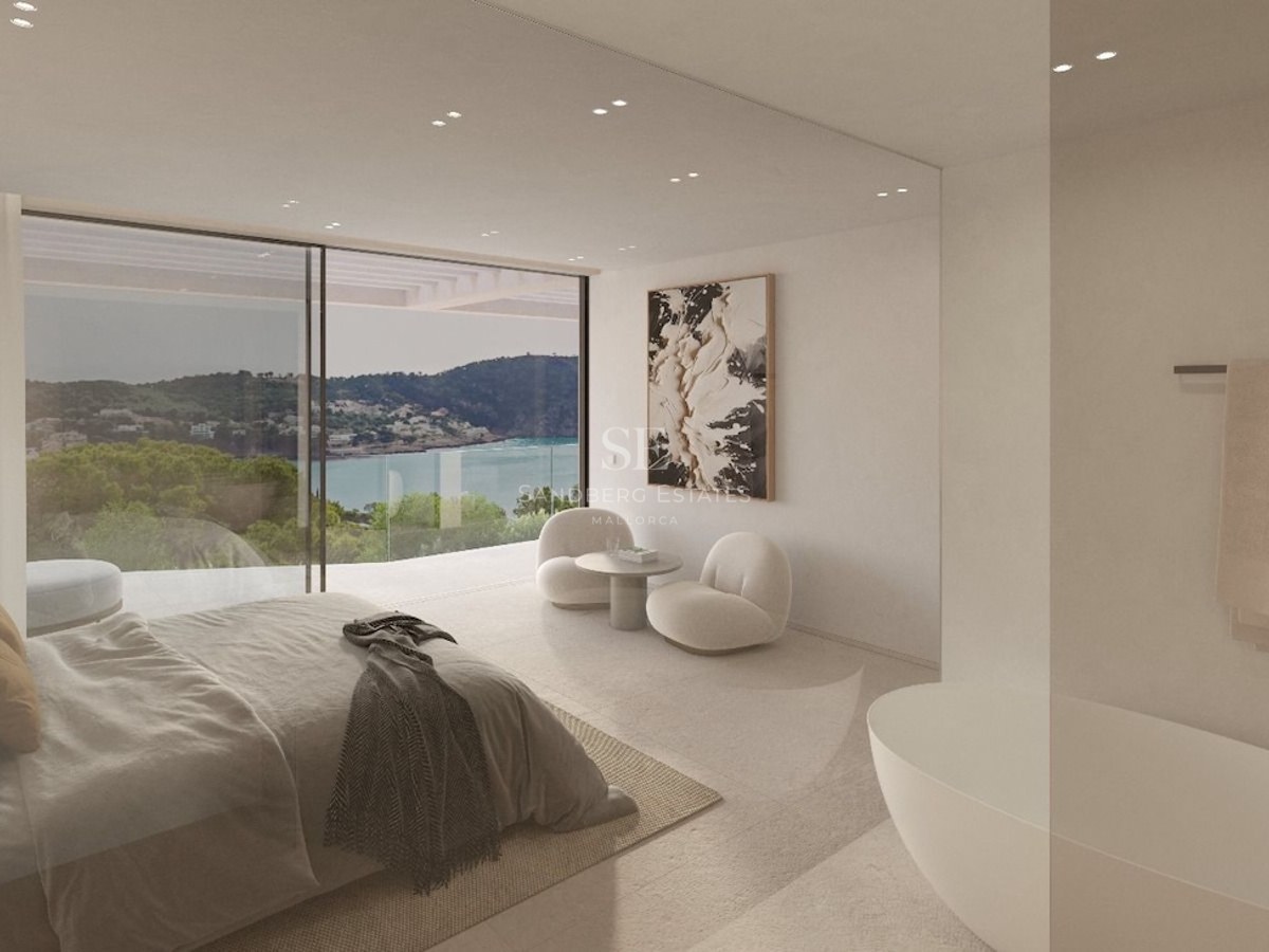 Modern bedroom with floor-to-ceiling windows overlooking a bay, featuring a freestanding tub and designer furniture.