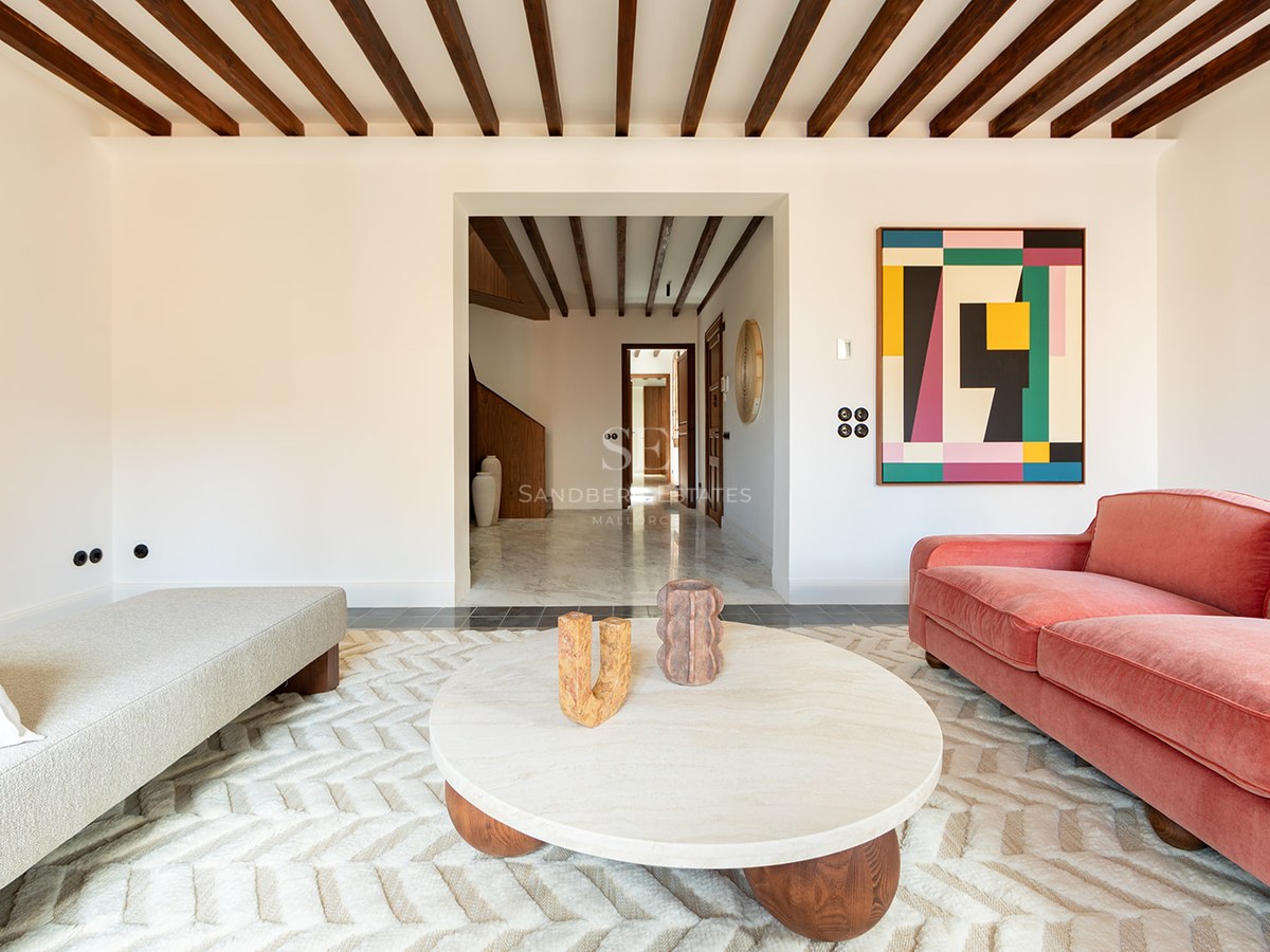 Modern living room featuring dark wood ceiling beams, a terracotta velvet sofa, marble coffee table, and textured rug.