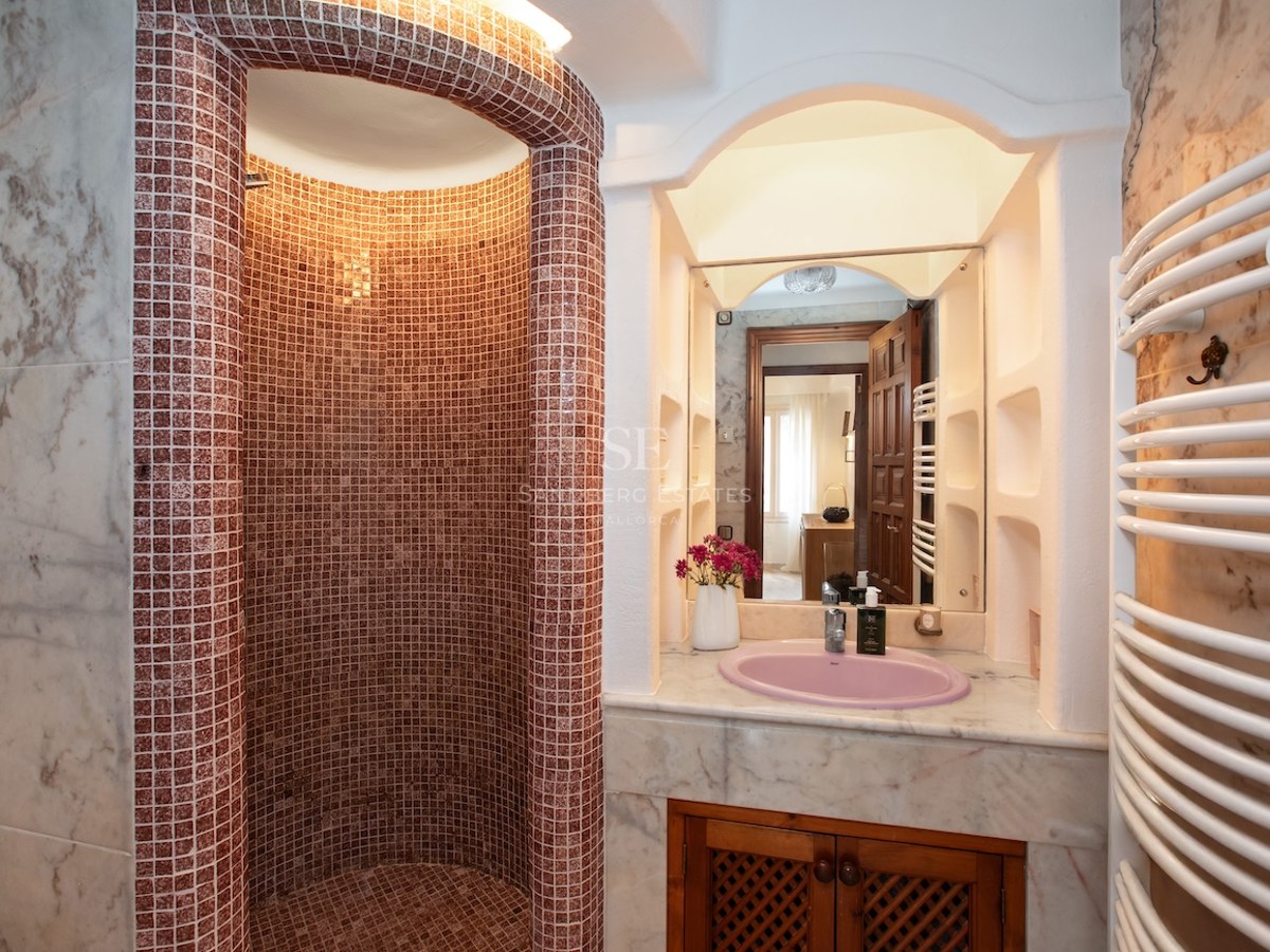 Douche à l'italienne courbe en mosaïque rougeâtre à côté d'un meuble vasque en marbre avec un évier rose.