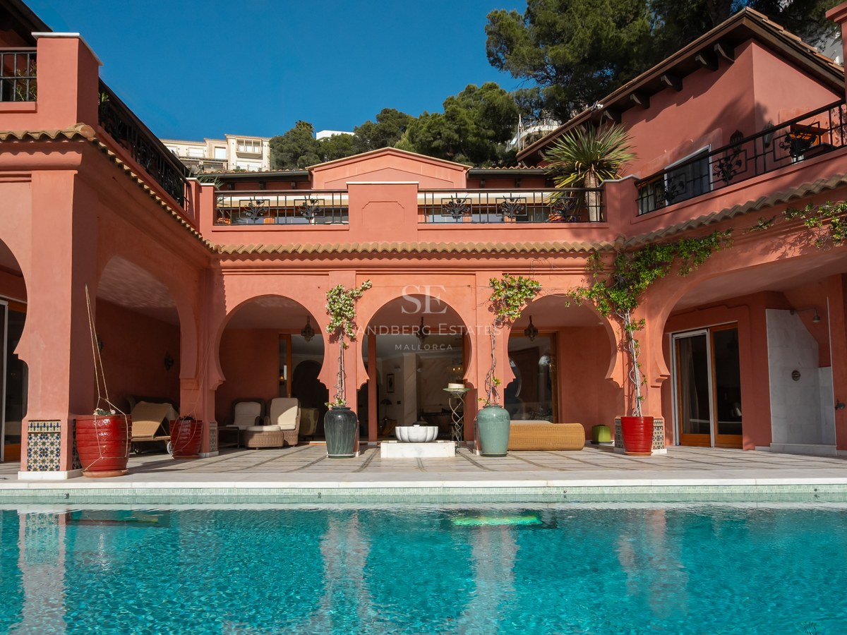 Façade de villa de luxe aux murs terre cuite avec arches mauresques donnant sur une piscine bleu turquoise.