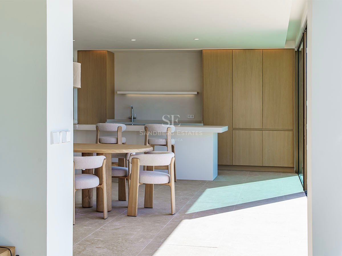 Cuisine moderne lumineuse avec placards en chêne clair, îlot en pierre blanche et table à manger circulaire en bois.