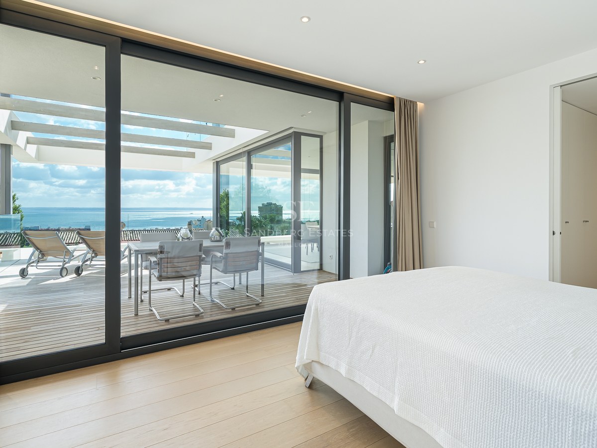 Chambre moderne avec lit blanc et grandes baies vitrées ouvrant sur une terrasse avec vue mer.