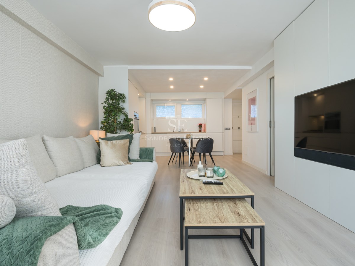 Bright modern living room featuring a white sofa, light wood floors, and a large flat-screen TV integrated into white cabinetry.