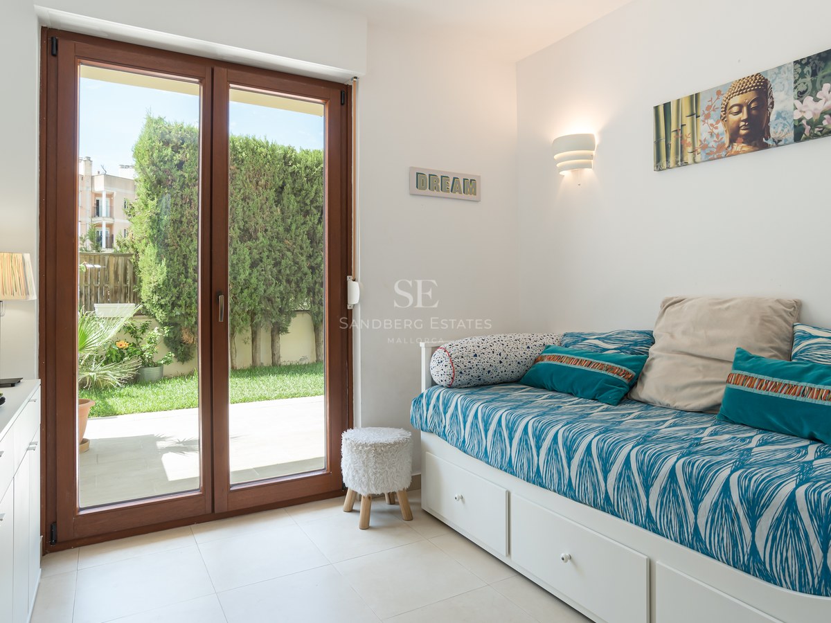 Dormitorio moderno con cama nido blanca y puertas correderas de madera hacia un jardín privado con setos verdes.