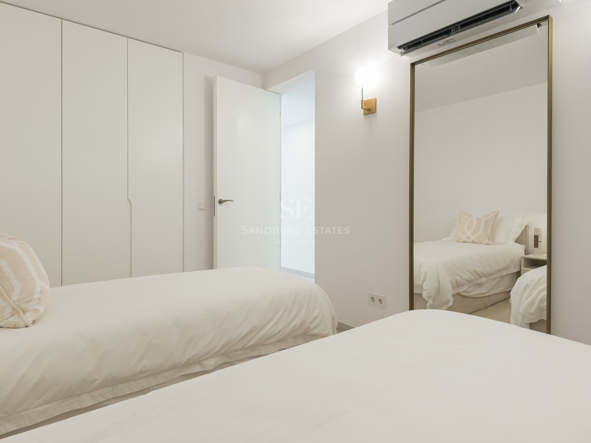 Bright minimalist bedroom featuring two twin beds, floor-to-ceiling white wardrobes, and a large gold-framed mirror.