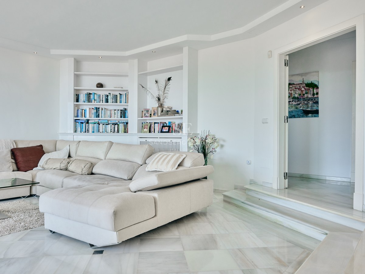 Contemporary living room with white marble floors, a large L-shaped cream sofa, and built-in white bookshelves.