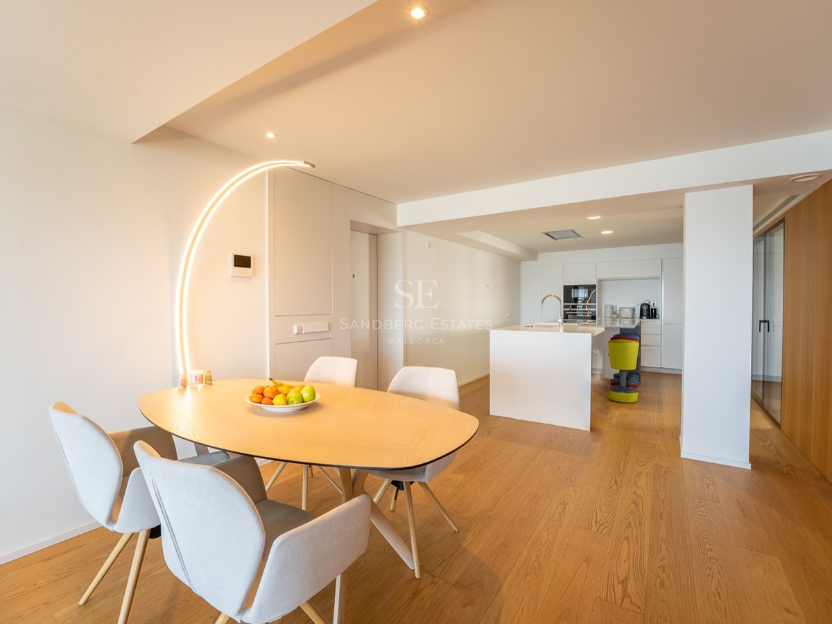 Salle à manger minimaliste avec table en bois clair, chaises grises et lampadaire arqué original.