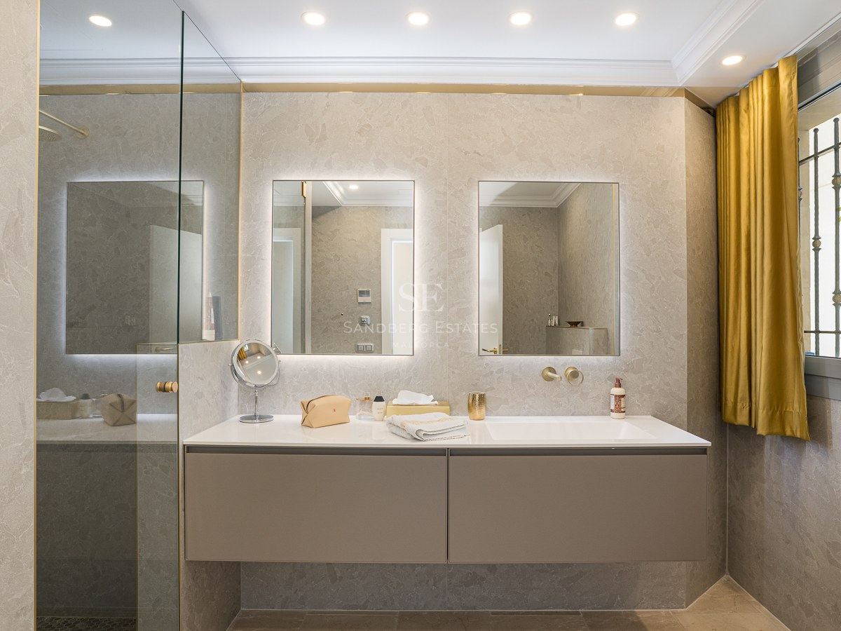 Contemporary bathroom featuring a floating taupe double vanity, twin backlit mirrors, and natural stone walls.