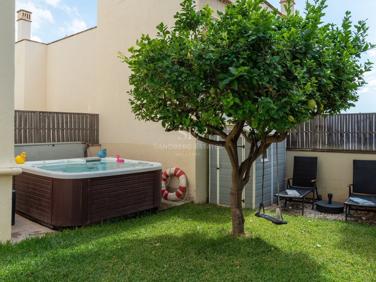 Pequeño jardín privado con césped, jacuzzi de madera, un limonero central y dos hamacas negras.