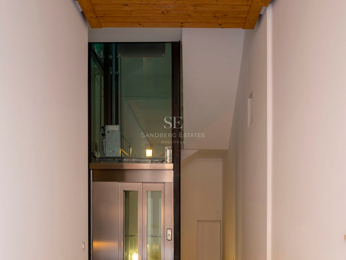 Modern hallway with stone mosaic flooring, wood ceiling, and a glass elevator at the end.