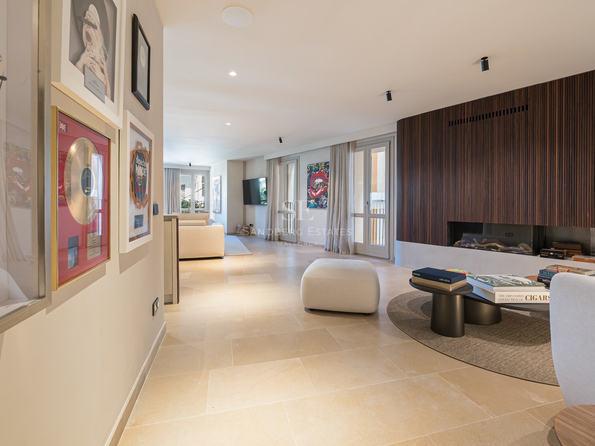 Modern living room featuring a wood-slat fireplace wall, stone floors, and framed music memorabilia in a hallway.
