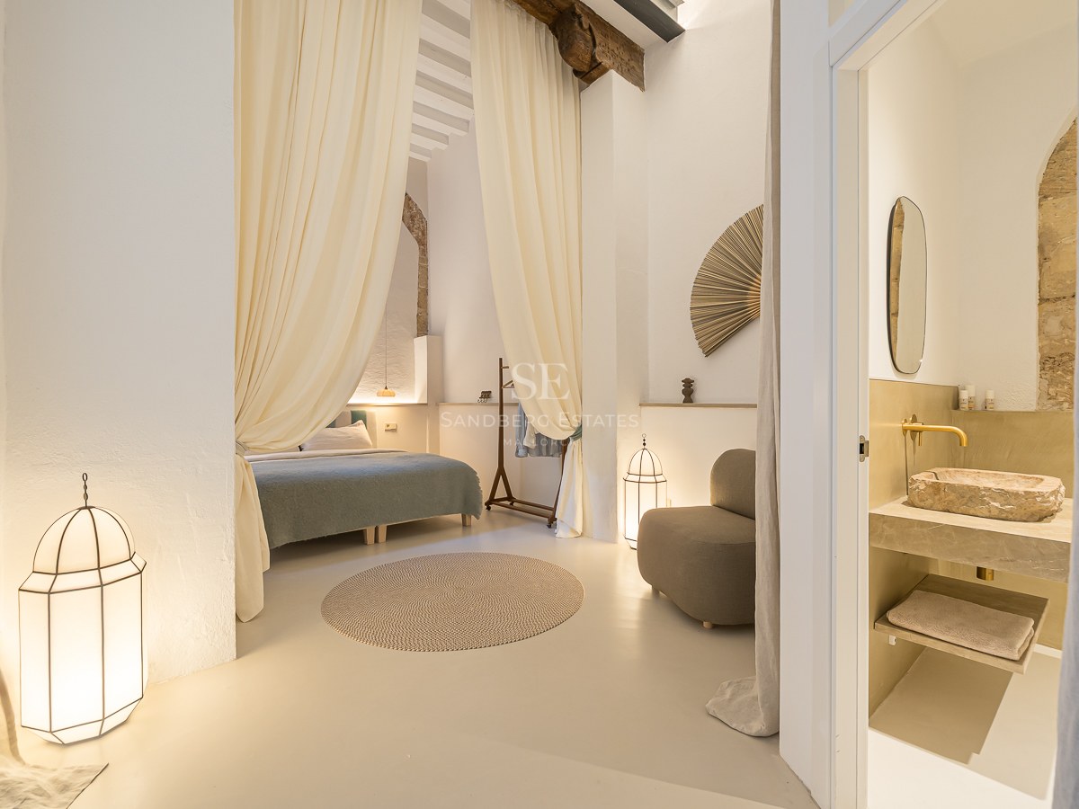 Chambre élégante avec des rideaux fluides, des poutres en bois, des lanternes et une salle de bain avec vasque en pierre.