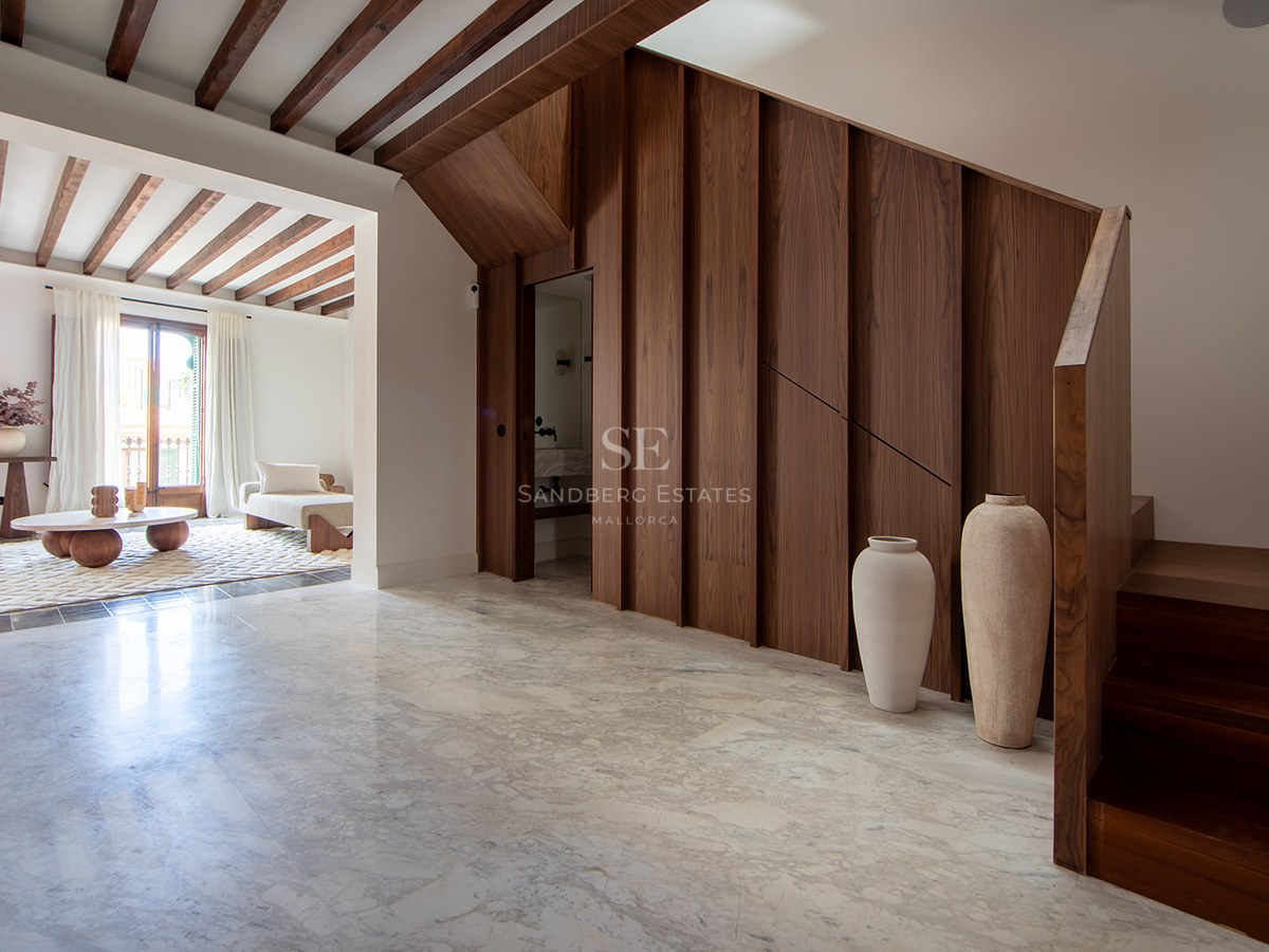 High-end hallway with marble floors, walnut wood paneling, exposed ceiling beams, and view of a sunlit living room.