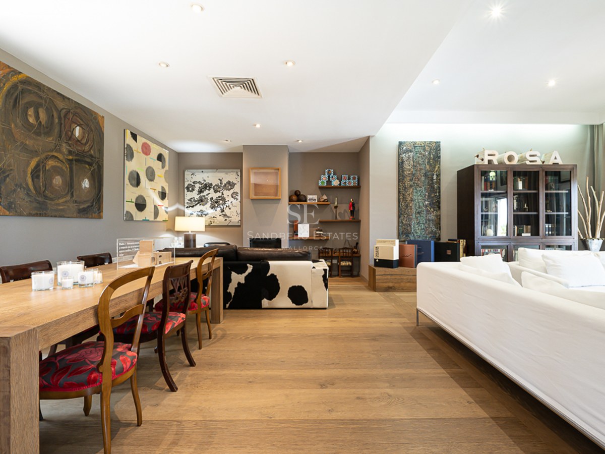 Grand salon avec parquet en chêne, art moderne, table à manger en bois et canapés blancs.