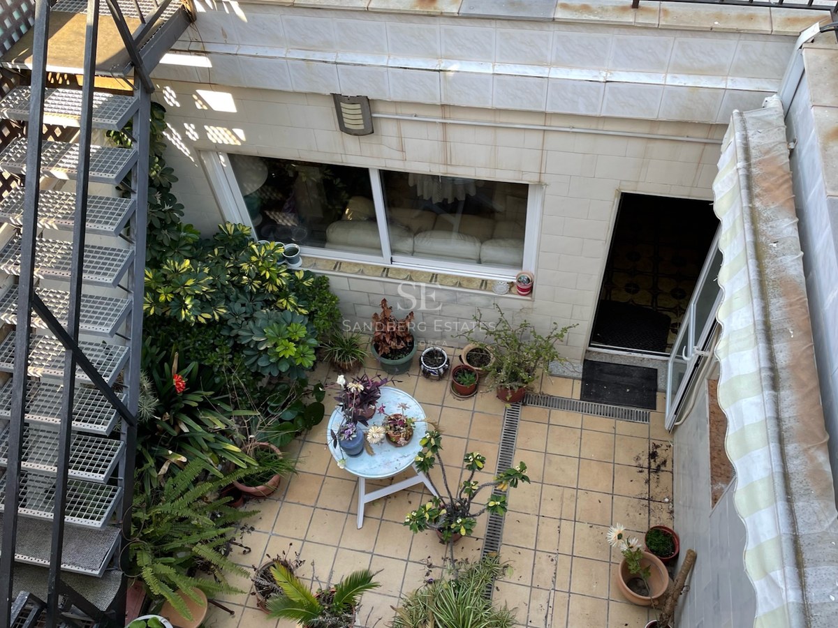 Vue d'en haut d'une terrasse carrelée avec escalier métallique, nombreuses plantes en pots et petite table ronde.