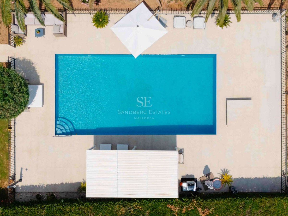 Aerial top-down view of a turquoise rectangular swimming pool surrounded by sand-colored stone decking and palm trees.