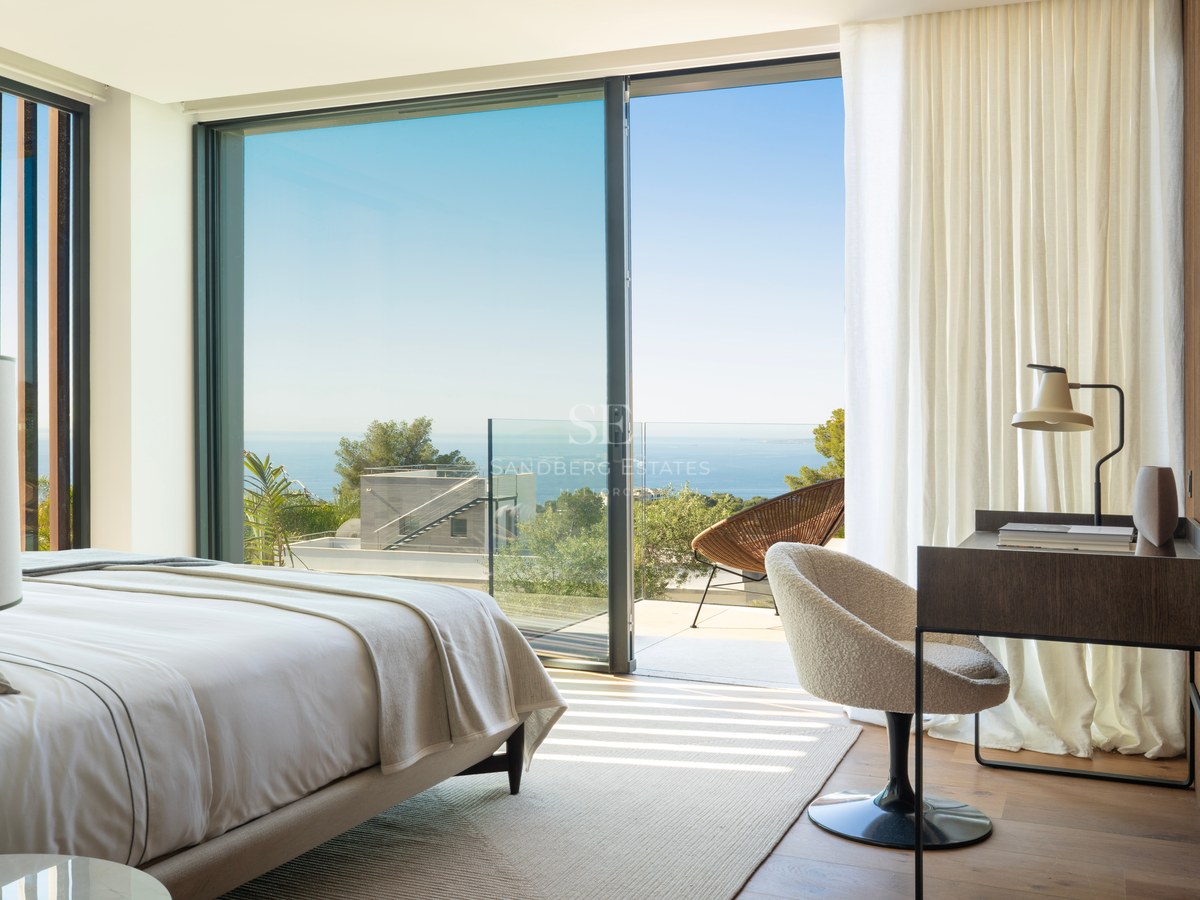 Chambre de maître moderne avec parquet, baies vitrées et terrasse offrant une vue sur la Méditerranée.