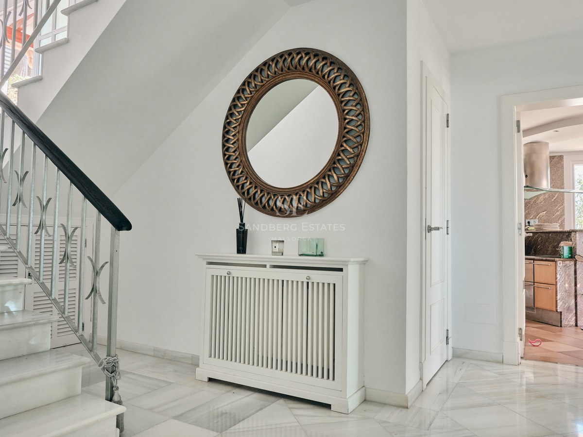 Bright entrance hall featuring marble stairs, a white radiator cover, and a large ornate gold circular mirror.