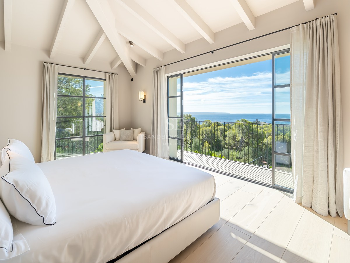 Bright master bedroom with vaulted white beamed ceiling, oak floors, and large glass doors to a sea view balcony.