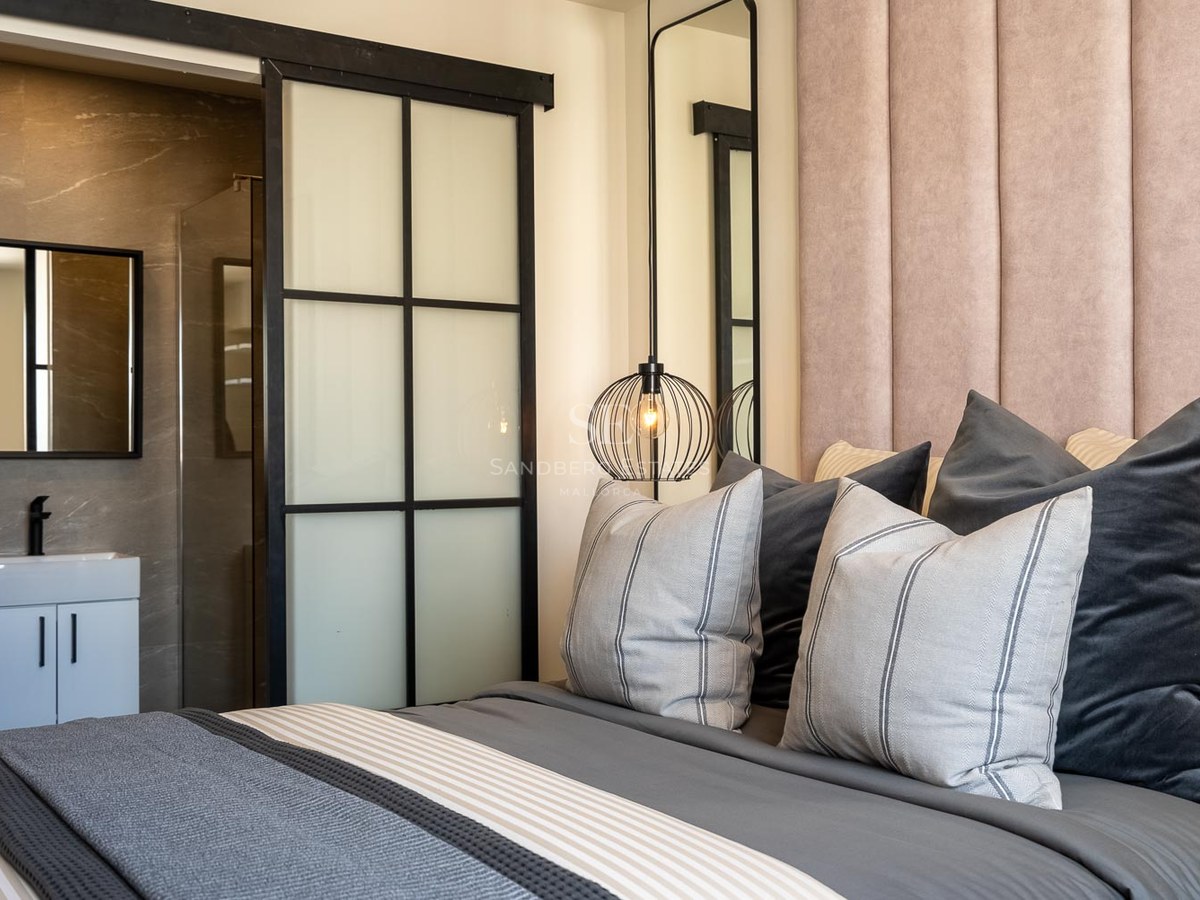 Chambre avec tête de lit en velours rose, luminaire design et porte coulissante industrielle menant à la salle de bain.