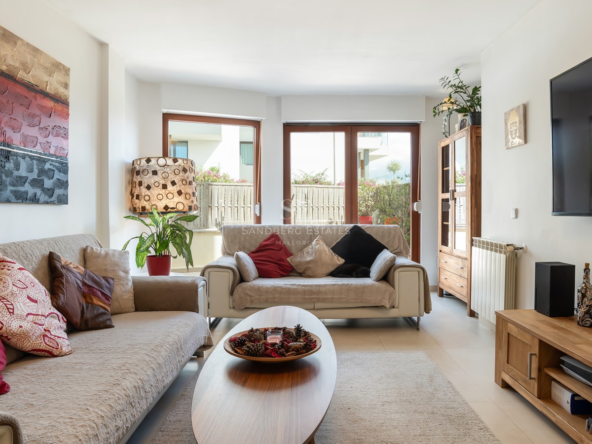 Salón iluminado con sofás beige, muebles de madera y grandes puertas de cristal que dan a una terraza privada.