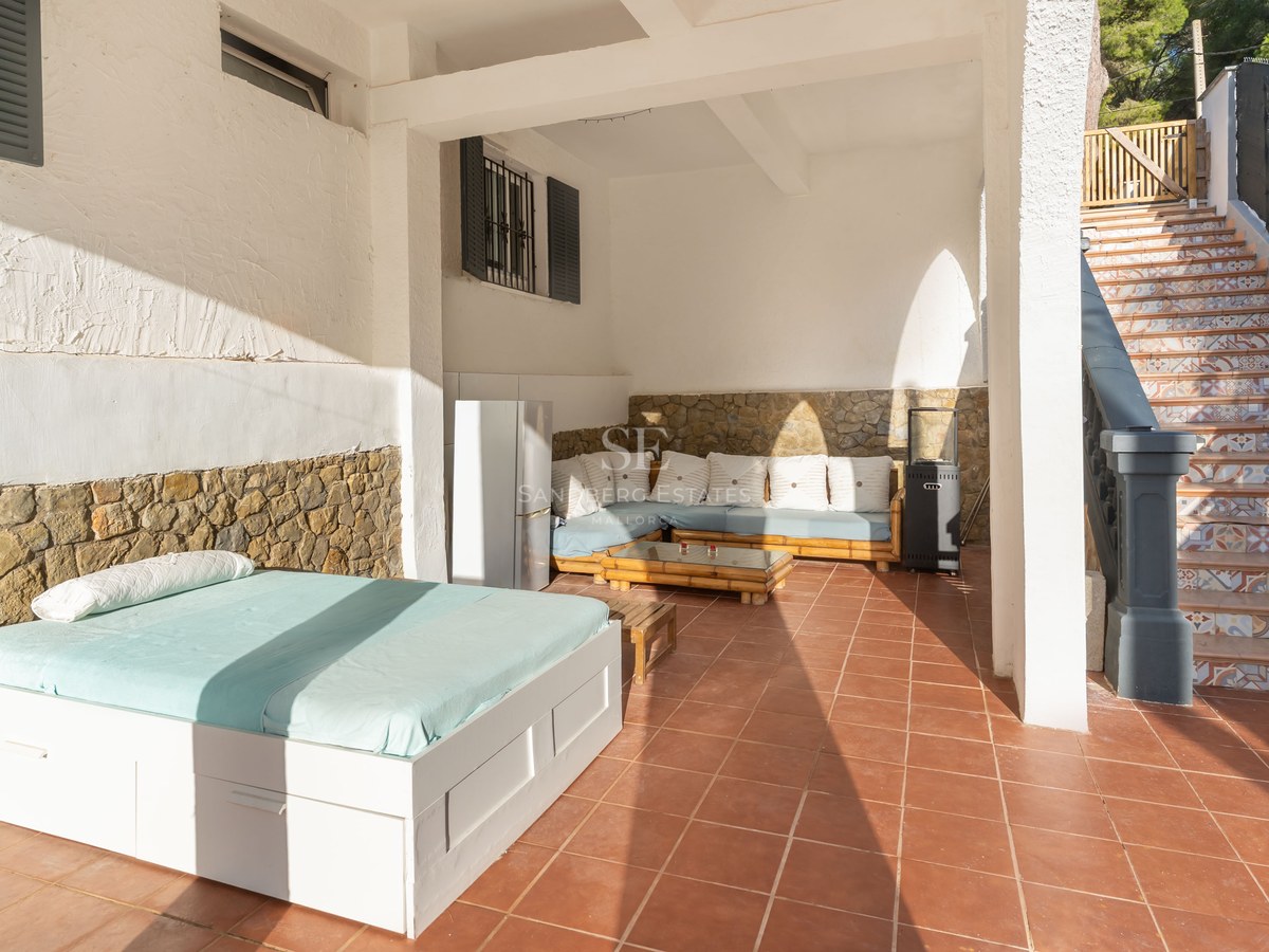 Covered terrace with terracotta floors, an outdoor daybed, lounge seating, stone walls, and stairs with patterned tiles.