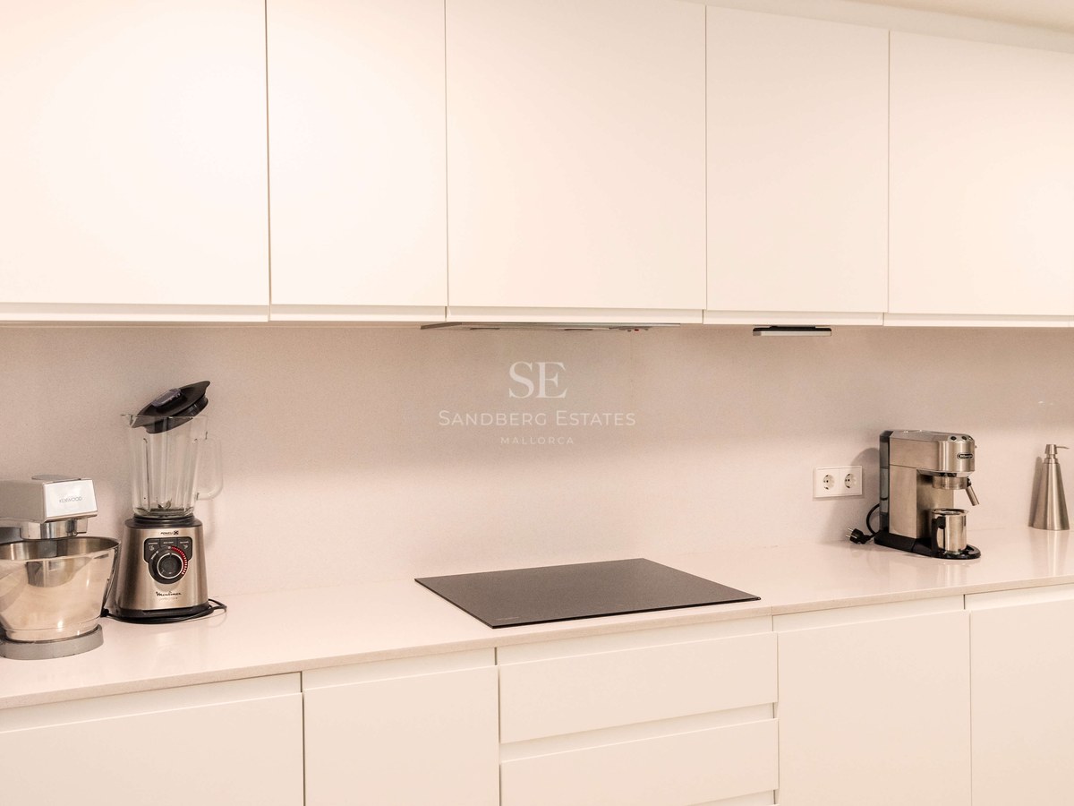 Cuisine blanche contemporaine avec placards sans poignées, plan de travail en quartz et plaque à induction.