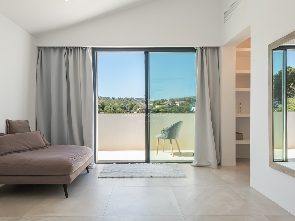 Modern bedroom featuring floor-to-ceiling glass doors opening to a sunlit terrace with landscape views.