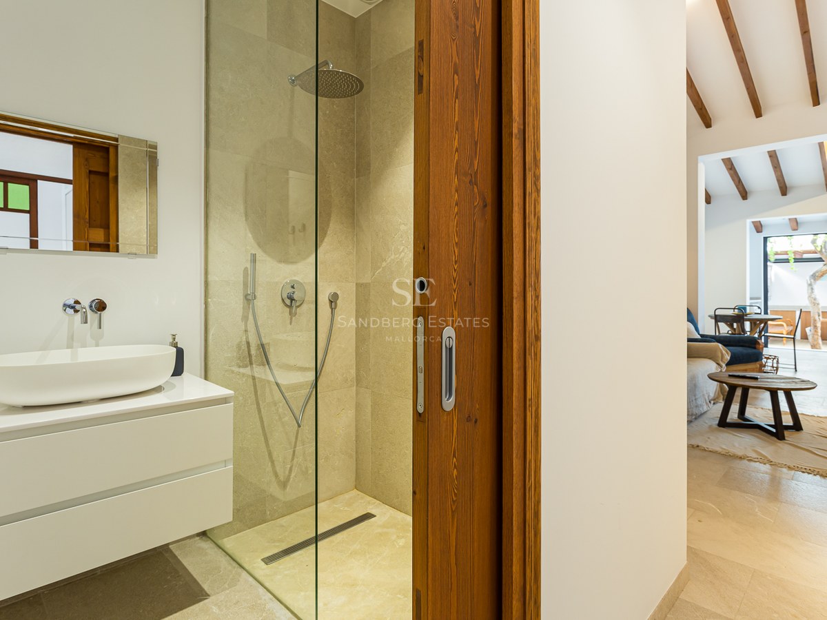Baño contemporáneo con ducha de piedra, lavabo sobre encimera blanco y puerta corredera de madera.