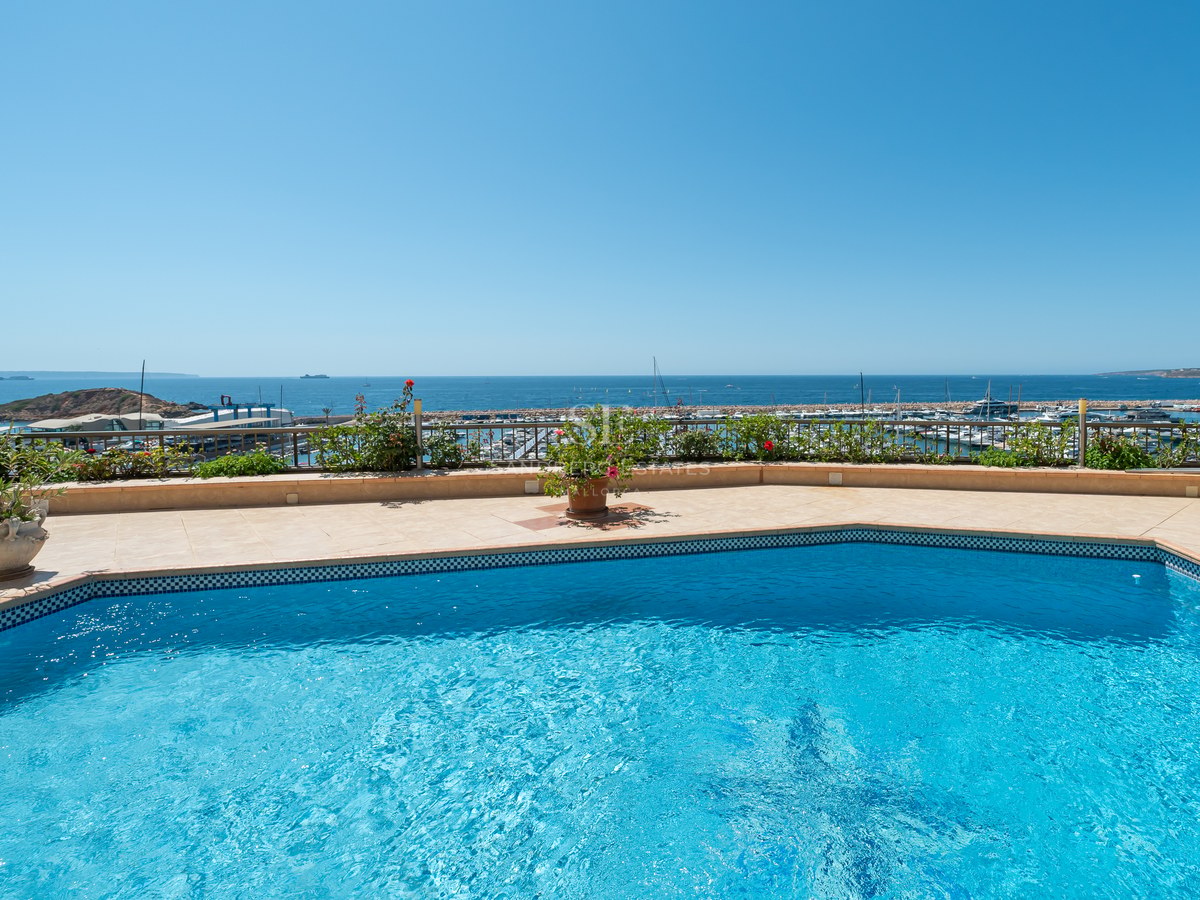 Luxury outdoor pool and stone terrace overlooking a Mediterranean marina and sea under a clear blue sky.