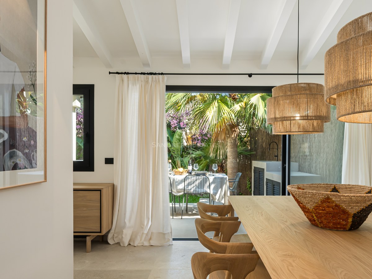 Salle à manger moderne avec table en chêne et suspensions en jute, s'ouvrant sur une terrasse de jardin luxuriante.