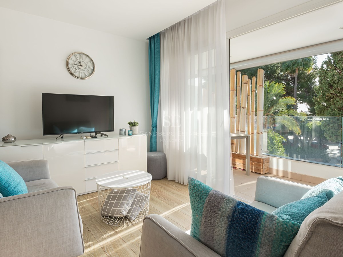 Modern living room with grey sofas, turquoise pillows, and large glass doors opening to a balcony with greenery.