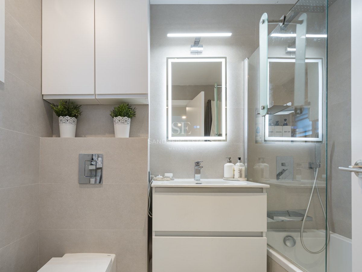 Modern bathroom with white vanity, backlit LED mirror, glass shower screen, and beige large-format tiles.