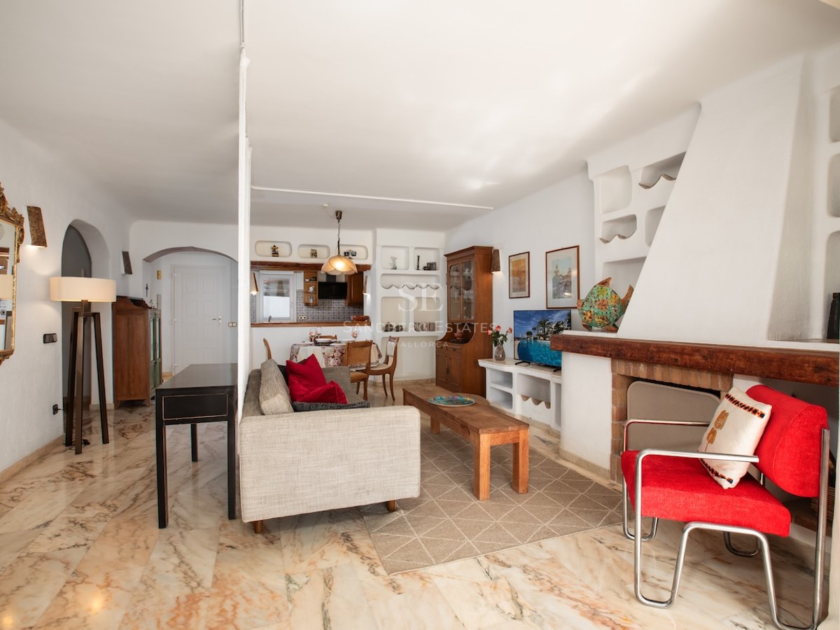 Salon lumineux avec sol en marbre poli, grande cheminée blanche, canapé gris et fauteuil rouge.