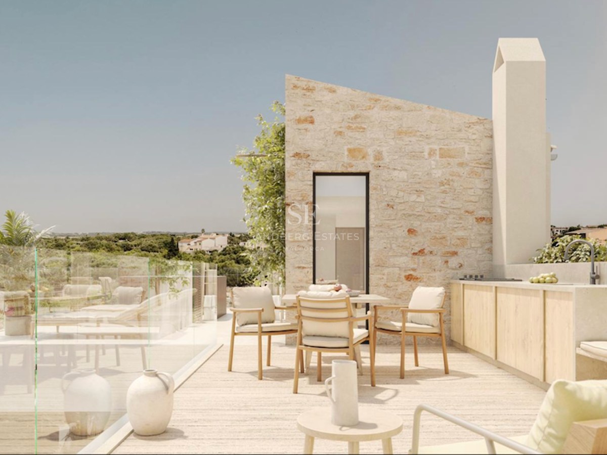 Terrasse moderne en pierre avec coin repas, cuisine extérieure et garde-corps en verre donnant sur la campagne.
