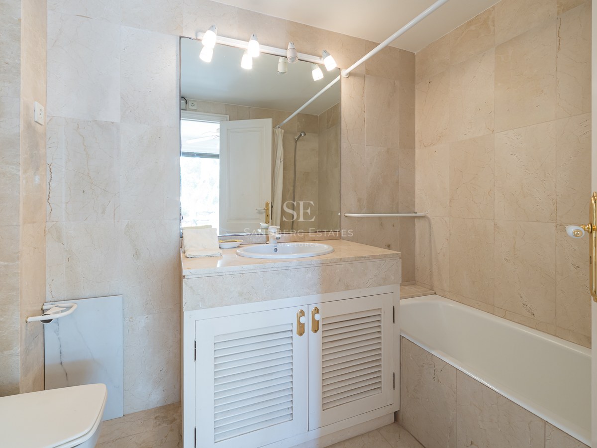 Salle de bains de style méditerranéen avec carrelage en marbre crème, baignoire intégrée et meuble vasque blanc.