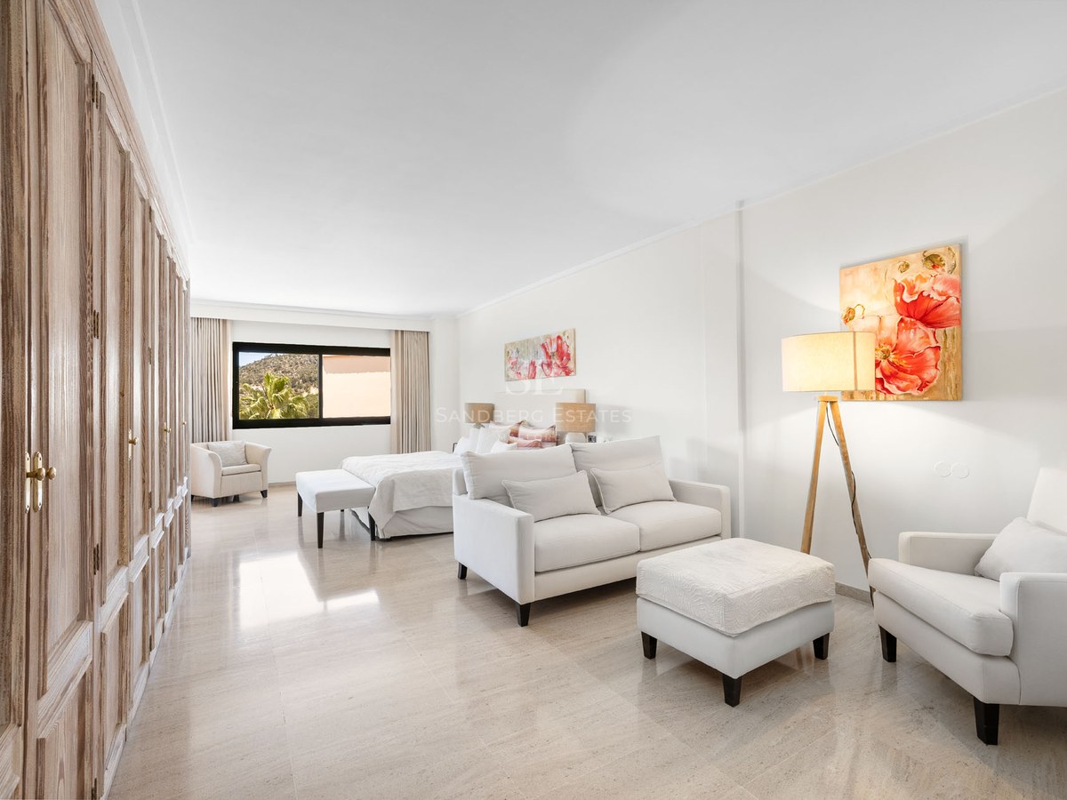 Suite lumineuse avec canapé blanc, armoires en bois, grand lit et art floral sur sol en marbre poli.